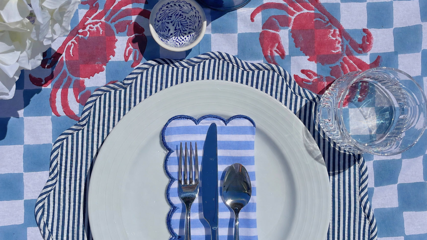 Table setting with blue and white checkered tablecloth, red crab print, striped placemat, and white plate with silverware.