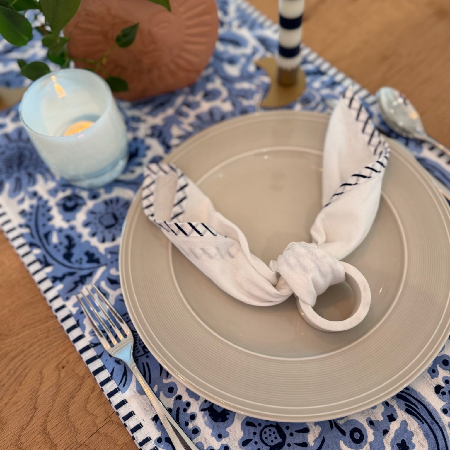 Table setting with beige plate, striped cloth, and candle on blue patterned tablecloth.